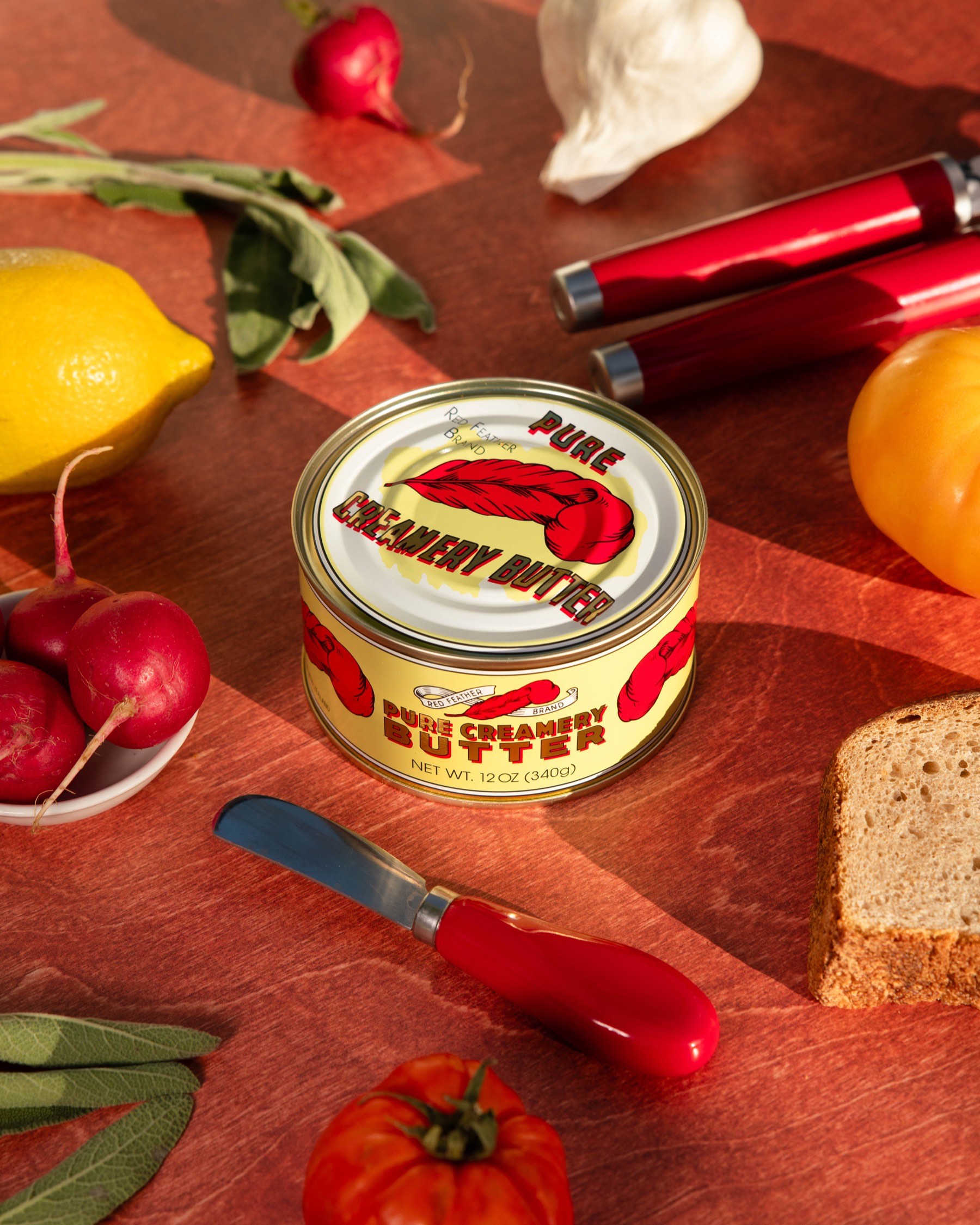A tin of Red Feather butter on a laid table with radishes, tomatoes, lemons and fresh bread