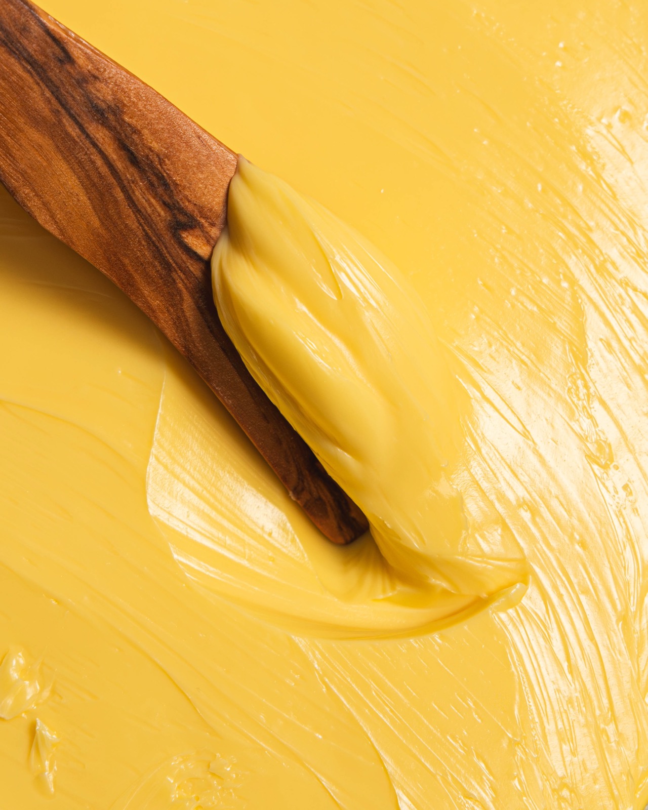 A wooden paddle drawn through freshly churned golden butter