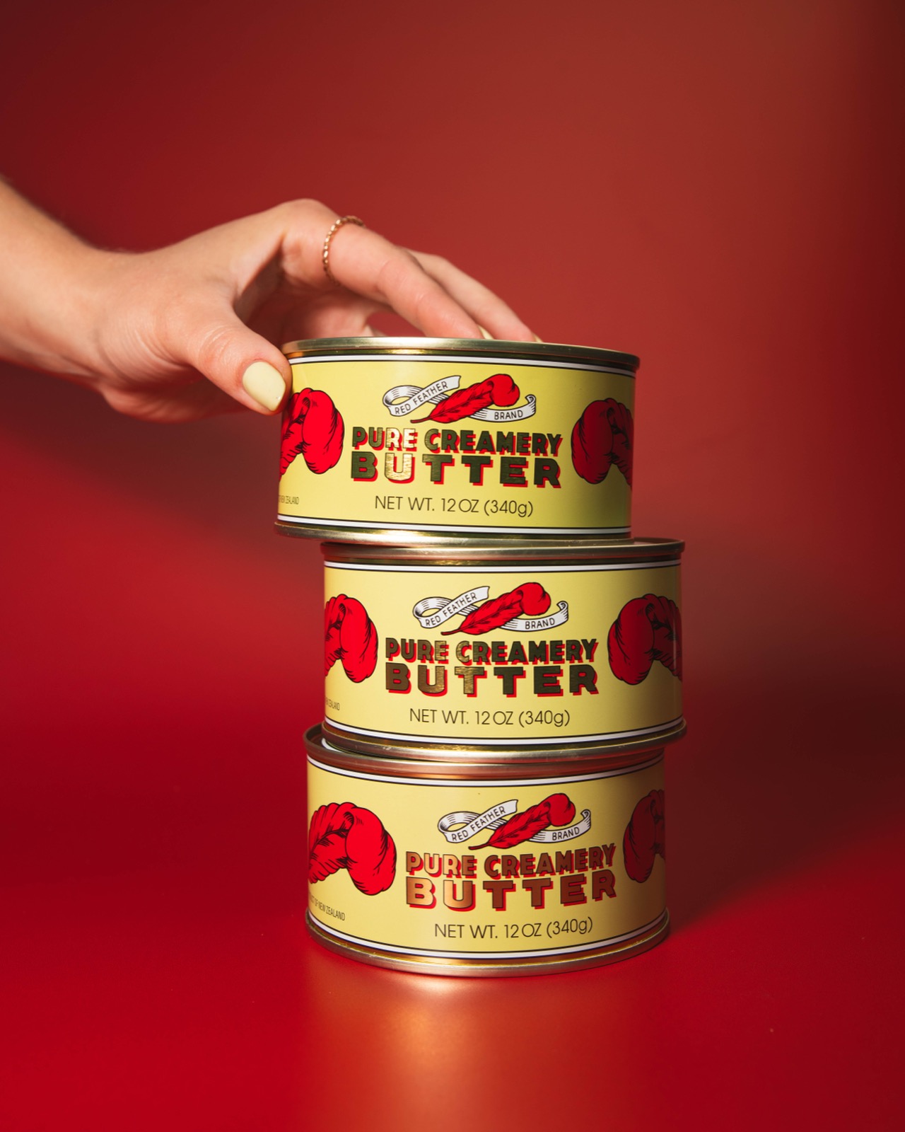Three stacked 12 ounce tins of Red Feather butter against a deep red background
